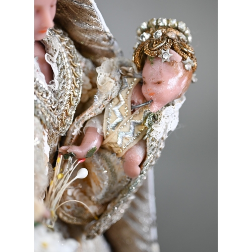 981 - A wax Madonna and Child figure in ornate embroidered and sequined robes, the plinth inscribed 'Monst... 