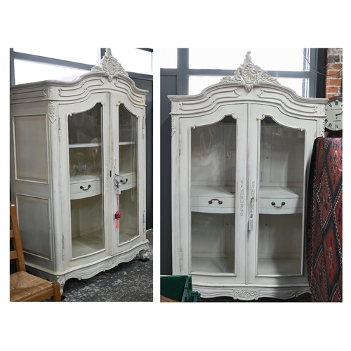 115 - Two Continental painted part glazed-in cabinets, of serpentine form with ornate carved pediment, wit... 