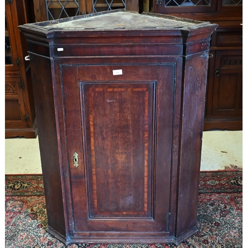 154 - An antique oak hanging corner cupboard with panelled door enclosing shelved interior, 80 cm wide x 1... 