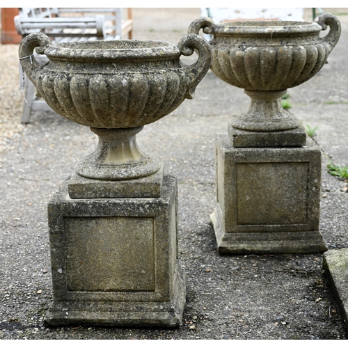 1 - A pair of weathered cast stone Regency style fluted twin handled urns, raised on square plinth bases... 