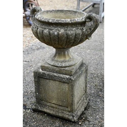 1 - A pair of weathered cast stone Regency style fluted twin handled urns, raised on square plinth bases... 