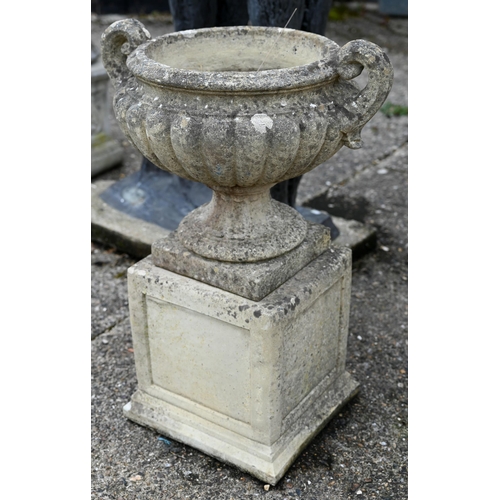 1 - A pair of weathered cast stone Regency style fluted twin handled urns, raised on square plinth bases... 