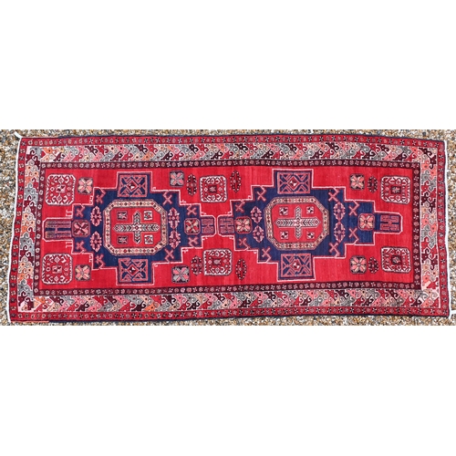 519 - A Persian red ground carpet with central geometric medallions and repeating borders, 337 x 142 cm