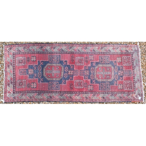 519 - A Persian red ground carpet with central geometric medallions and repeating borders, 337 x 142 cm