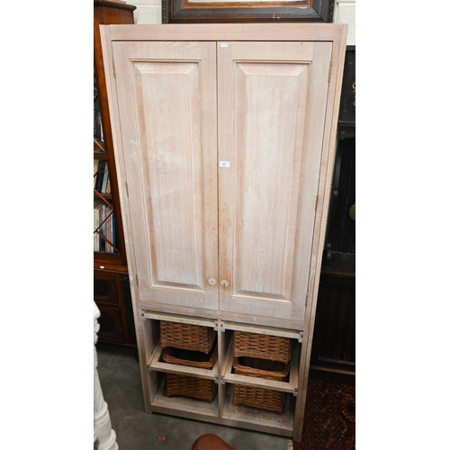 81 - A limed ash pantry cupboard with panelled doors enclosing two shelves (missing brackets) over four b... 