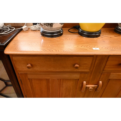 77 - A mid-century Ercol elm and beech sideboard with two drawers and panelled cupboards raised on splaye... 