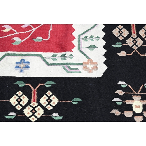 620 - A mid-century Caucasian design Kelim carpet, the stylised floral design on red/black ground, 360 cm ... 