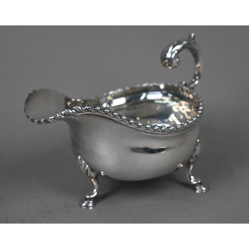 100 - A silver sauce boat in the Georgian manner, with gadrooned rim and scroll handle, on three hoof feet... 