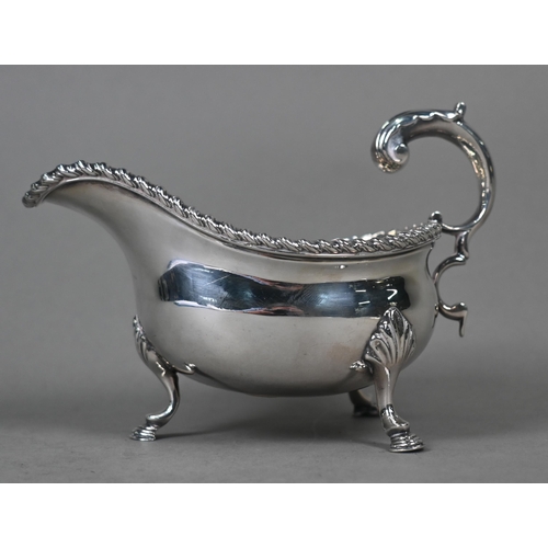 100 - A silver sauce boat in the Georgian manner, with gadrooned rim and scroll handle, on three hoof feet... 