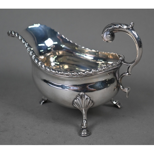 100 - A silver sauce boat in the Georgian manner, with gadrooned rim and scroll handle, on three hoof feet... 