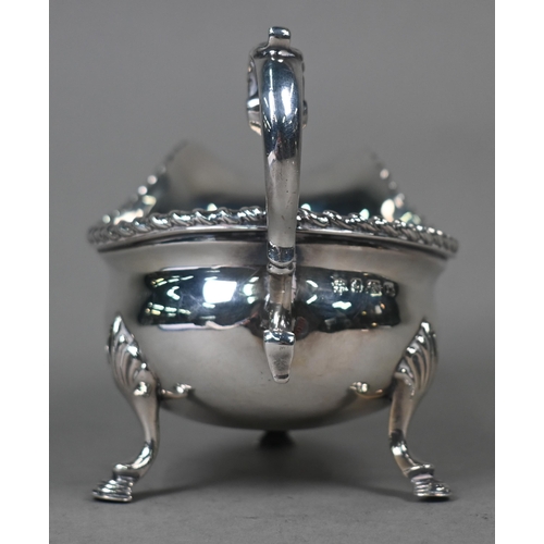 100 - A silver sauce boat in the Georgian manner, with gadrooned rim and scroll handle, on three hoof feet... 