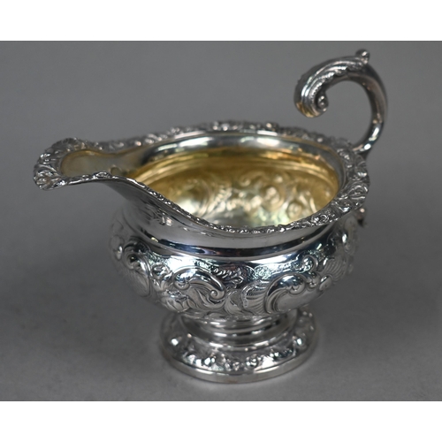 115 - A George IV silver milk jug in the Regency manner, with embossed and chased decoration and scroll ha... 