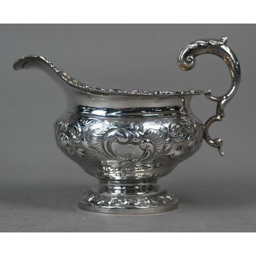 115 - A George IV silver milk jug in the Regency manner, with embossed and chased decoration and scroll ha... 