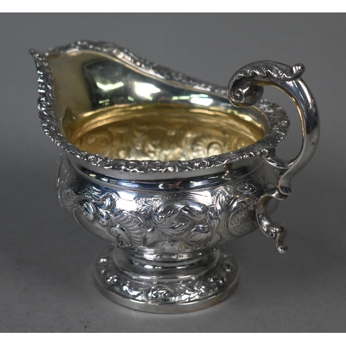 115 - A George IV silver milk jug in the Regency manner, with embossed and chased decoration and scroll ha... 