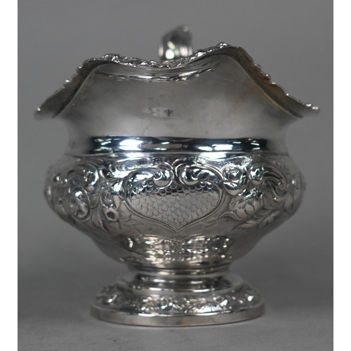 115 - A George IV silver milk jug in the Regency manner, with embossed and chased decoration and scroll ha... 