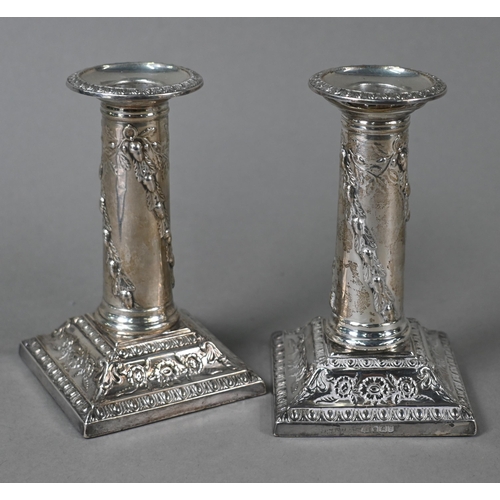 27 - A late Victorian pair of loaded silver candlesticks with embossed pillars and moulded square bases, ... 