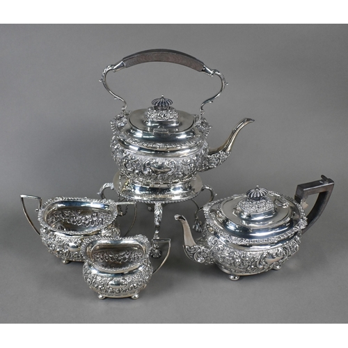 63 - An Edwardian silver four-piece tea service including kettle on stand, with embossed and chased decor... 