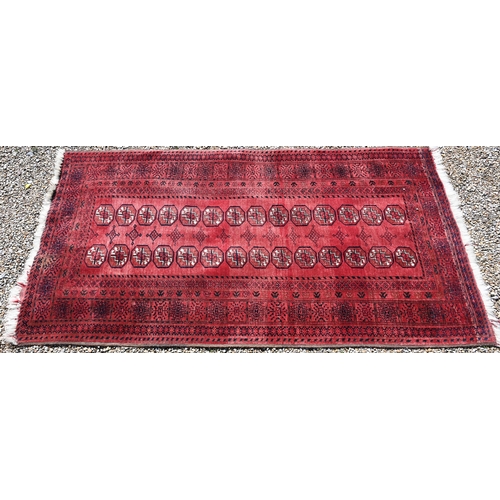 627 - An old Afghan red ground rug, the field with two rows of geometric guls, 207 cm x 106 cm, even wear,... 