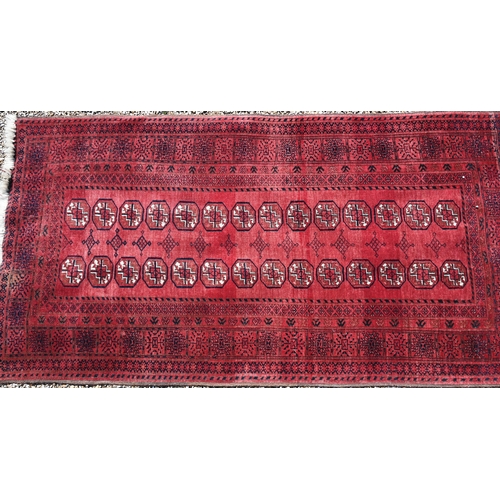 627 - An old Afghan red ground rug, the field with two rows of geometric guls, 207 cm x 106 cm, even wear,... 