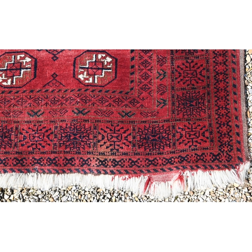 627 - An old Afghan red ground rug, the field with two rows of geometric guls, 207 cm x 106 cm, even wear,... 