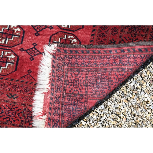 627 - An old Afghan red ground rug, the field with two rows of geometric guls, 207 cm x 106 cm, even wear,... 