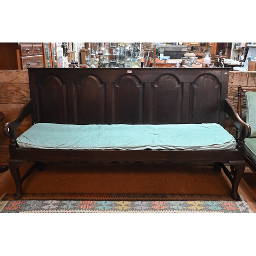 700 - A George III oak settle, the five arched panel back over shaped arms, raised on cabriole front legs,... 