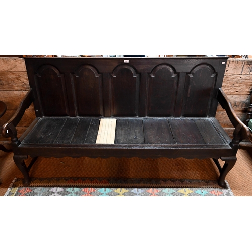 700 - A George III oak settle, the five arched panel back over shaped arms, raised on cabriole front legs,... 