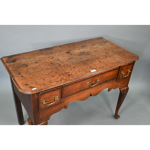 730 - An 18th century oak three drawer lowboy within a shaped apron, raised on cabriole legs to pad feet, ... 