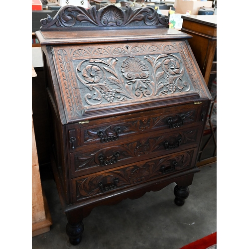 28 - A carved oak bureau with fall front panel enclosing fitted interior over three drawers on turned sup... 