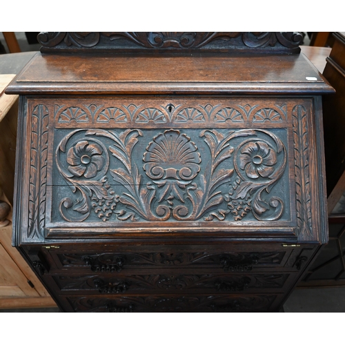 28 - A carved oak bureau with fall front panel enclosing fitted interior over three drawers on turned sup... 