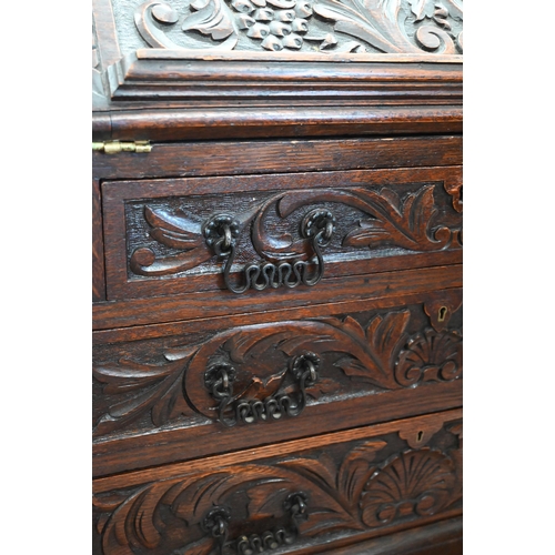 28 - A carved oak bureau with fall front panel enclosing fitted interior over three drawers on turned sup... 