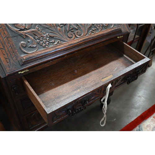 28 - A carved oak bureau with fall front panel enclosing fitted interior over three drawers on turned sup... 