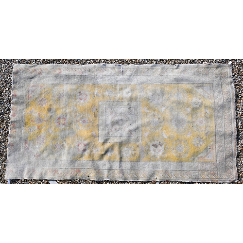 182 - A Chinese design very worn/faded yellow ground rug with bats and floral roundels scattered around ce... 