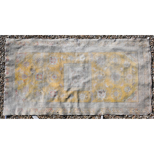 182 - A Chinese design very worn/faded yellow ground rug with bats and floral roundels scattered around ce... 