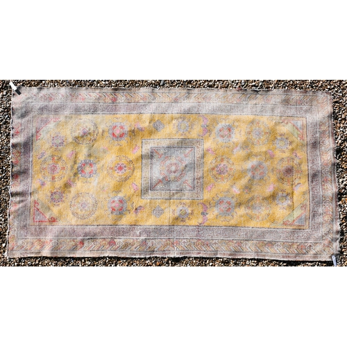 182 - A Chinese design very worn/faded yellow ground rug with bats and floral roundels scattered around ce... 