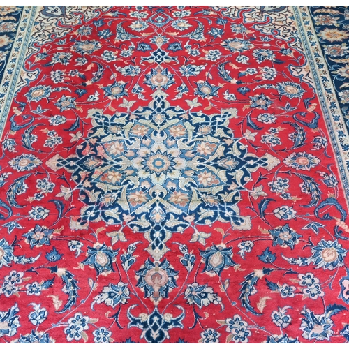 10 - A Persian Mashad carpet with traditional floral design on red ground, navy blue palmette pattern bor... 