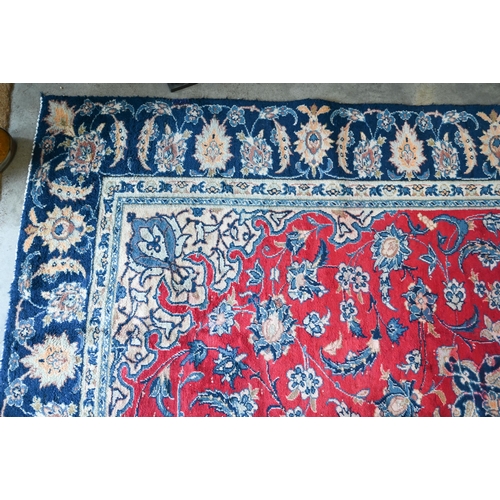 10 - A Persian Mashad carpet with traditional floral design on red ground, navy blue palmette pattern bor... 