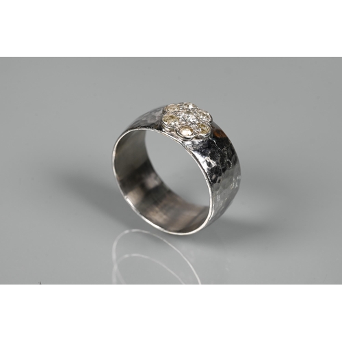 231 - A contemporary 9ct white gold wide band with hammered finish, set with seven-stone diamond cluster, ... 