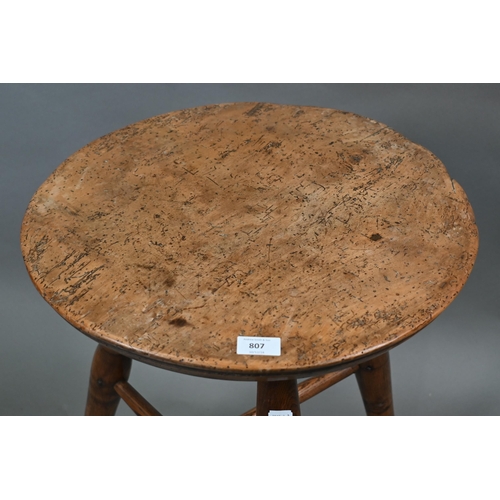 807 - An antique walnut and elm cricket table, the circular top raised on three turned legs united by a t-... 