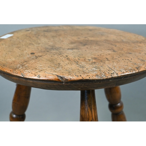 807 - An antique walnut and elm cricket table, the circular top raised on three turned legs united by a t-... 