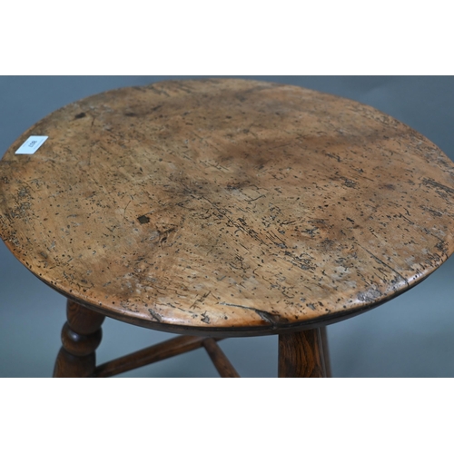 807 - An antique walnut and elm cricket table, the circular top raised on three turned legs united by a t-... 