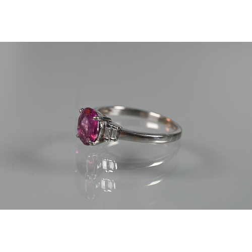 190 - A pink sapphire and diamond ring, the central oval claw set pink sapphire flanked by two graduated b... 