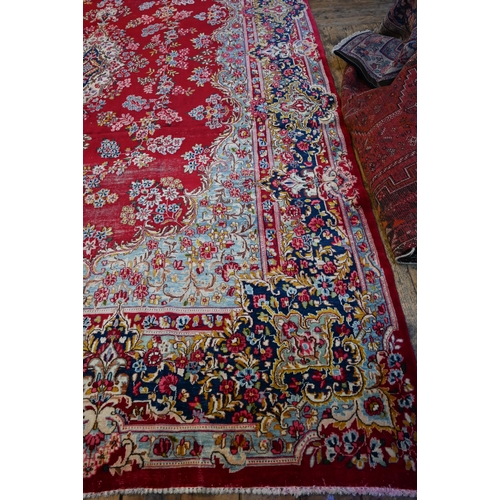 774 - A large Persian Kerman red ground carpet with traditional floral design around the central medalion,... 