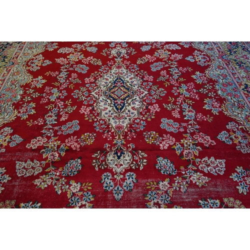 774 - A large Persian Kerman red ground carpet with traditional floral design around the central medalion,... 