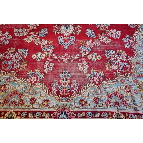 774 - A large Persian Kerman red ground carpet with traditional floral design around the central medalion,... 