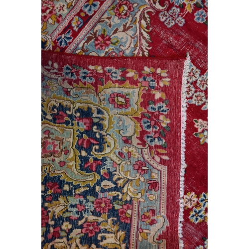 774 - A large Persian Kerman red ground carpet with traditional floral design around the central medalion,... 