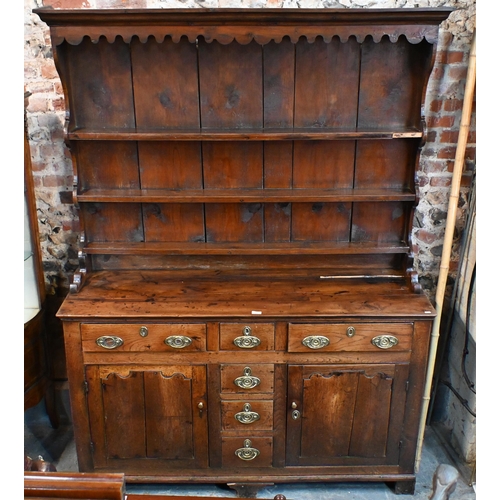 883 - An 18th century fruitwood and oak/elm dresser, the wavy cornice top with plank back over three shelv... 