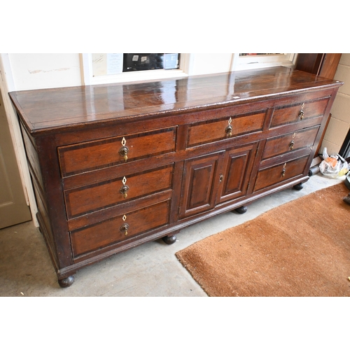 162 - An 18th century oak sideboard with seven drawers arranged around the pair of central cupboard doors ... 