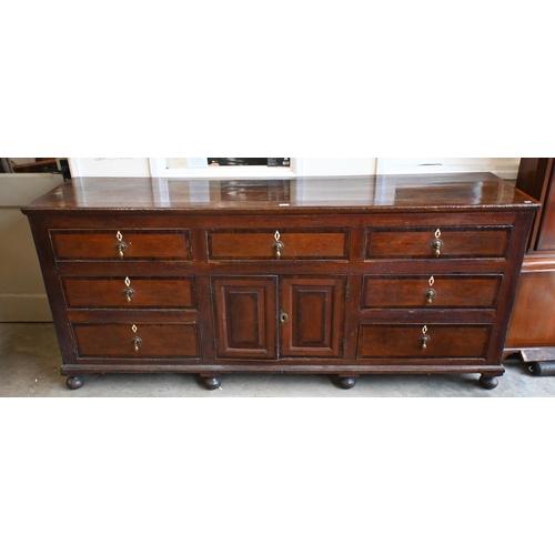 162 - An 18th century oak sideboard with seven drawers arranged around the pair of central cupboard doors ... 