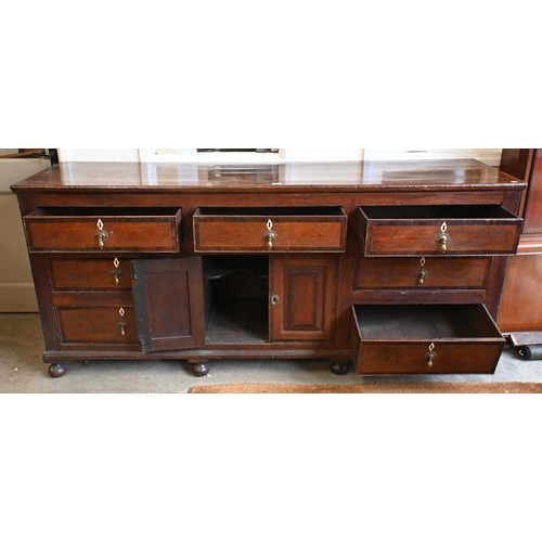 162 - An 18th century oak sideboard with seven drawers arranged around the pair of central cupboard doors ... 